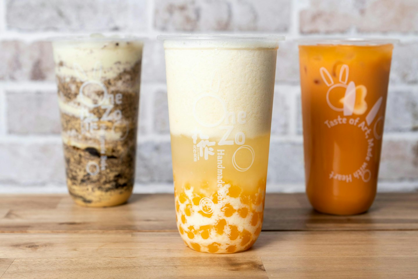 Na dřevěném stole stojí tři barevné bubble tea nápoje.
