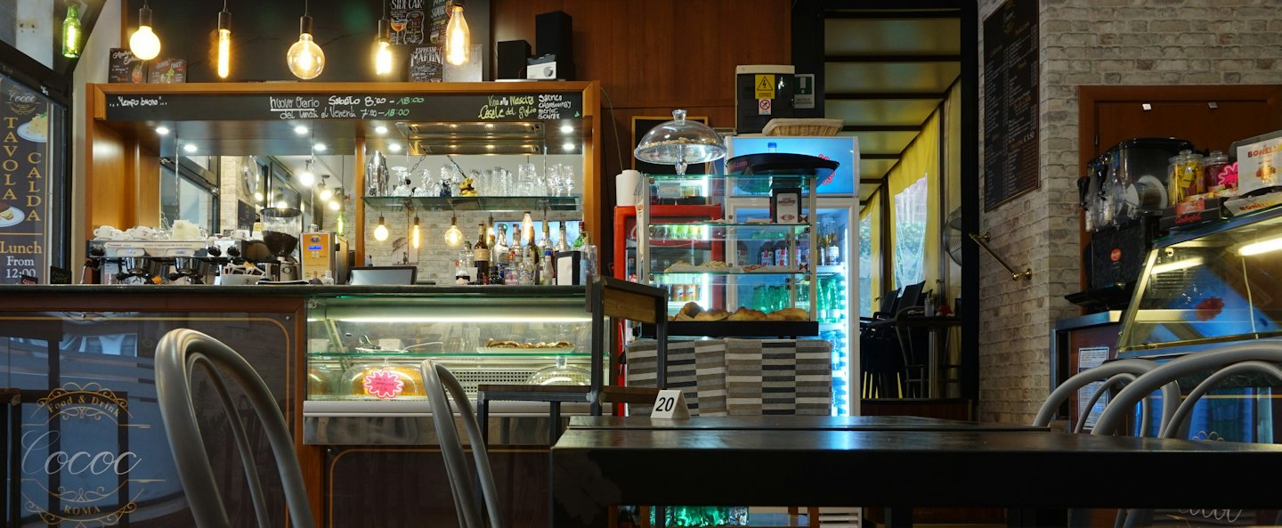 Moderní interiér kavárny s espresso automaty a dřevěnými stoly.