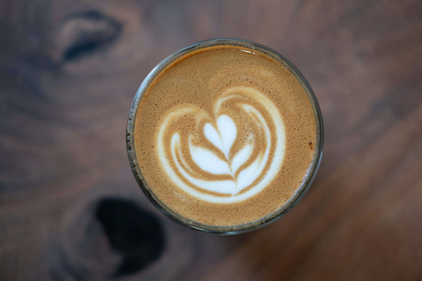Latte art ve skleněném šálku na dřevěném stole.